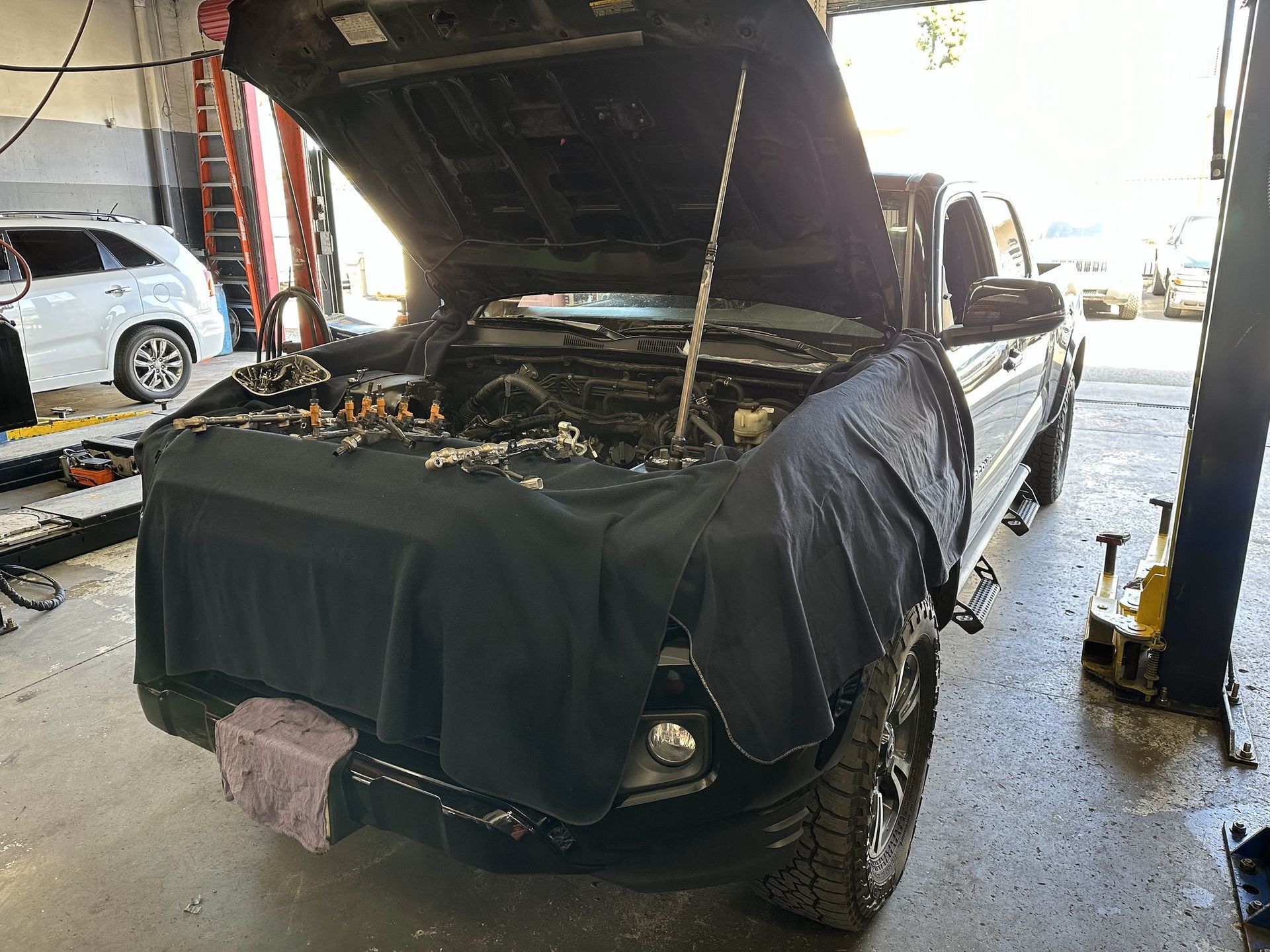 Black truck with open hood in a garage. Mechanic's protective cover on the front.