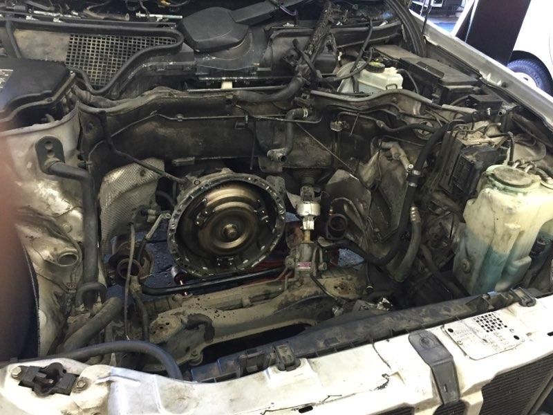 Car engine bay with parts removed, revealing engine components. Black, silver, and dirty.