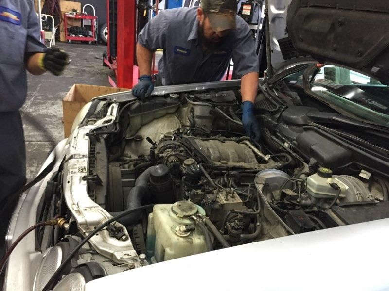 Mechanic working on a car engine in a garage; hood open.