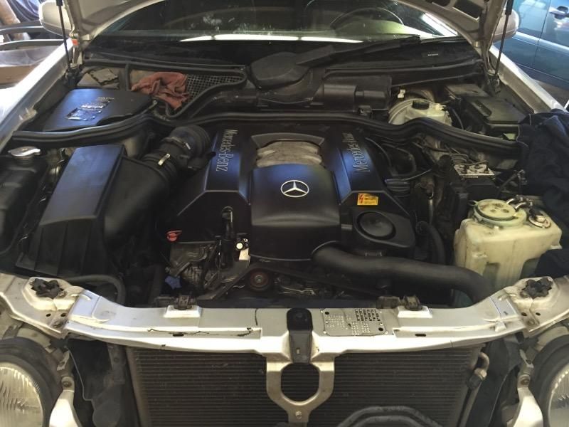 Car engine bay with open hood. Silver car, black engine cover with Mercedes logo.