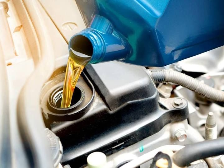 Pouring oil into a car engine. Yellow oil flows from a blue container into a black engine compartment.