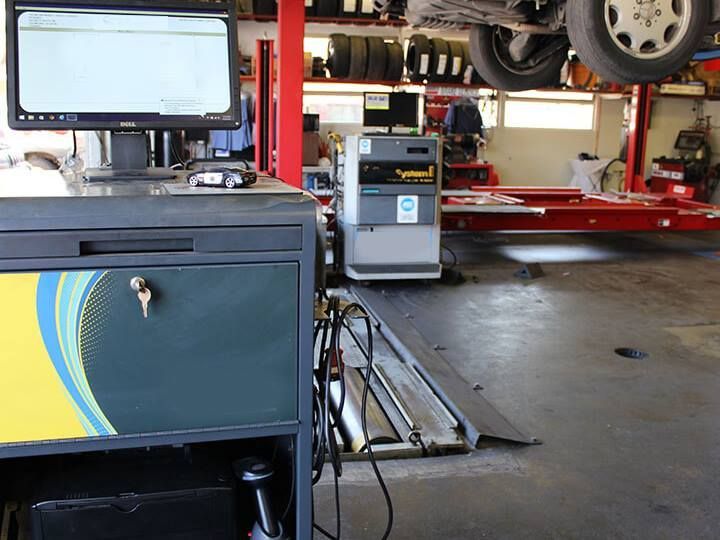 A car on a lift in a repair shop. Diagnostic equipment and computer are in the foreground.
