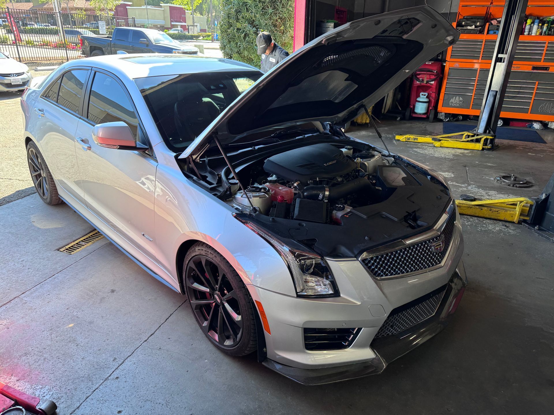 Silver sedan with hood open at an auto shop, showing exposed engine and black wheels.
