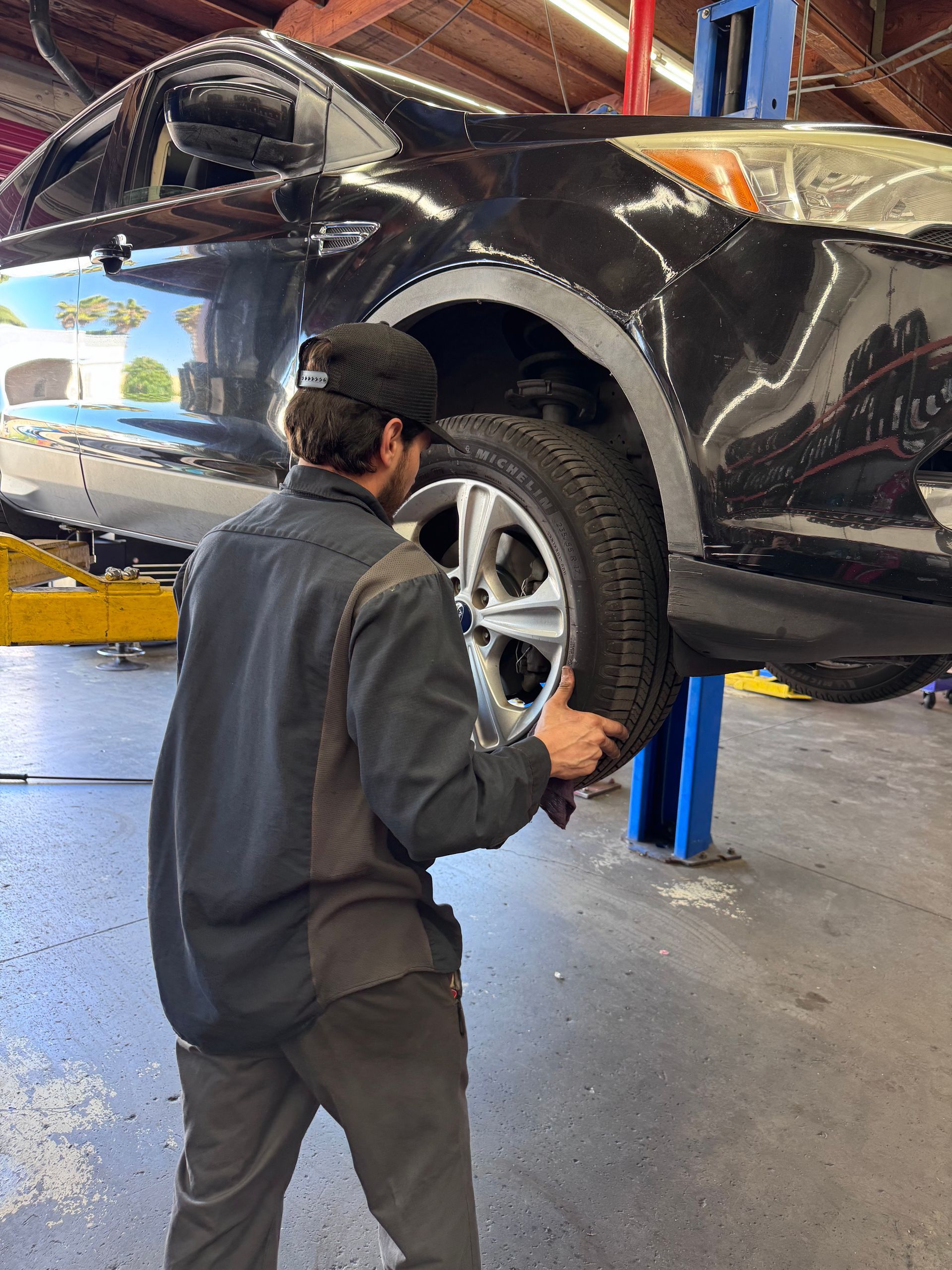 Mechanic inspecting the rear wheel of a black car in an auto repair shop.