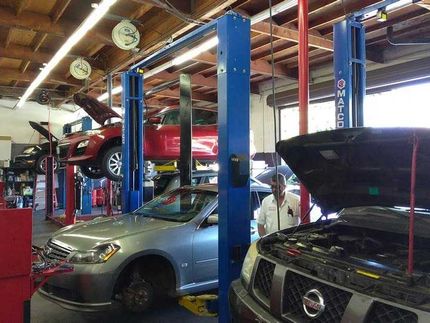 Cars on lifts in a busy auto repair shop, a mechanic standing near an open-hooded vehicle.