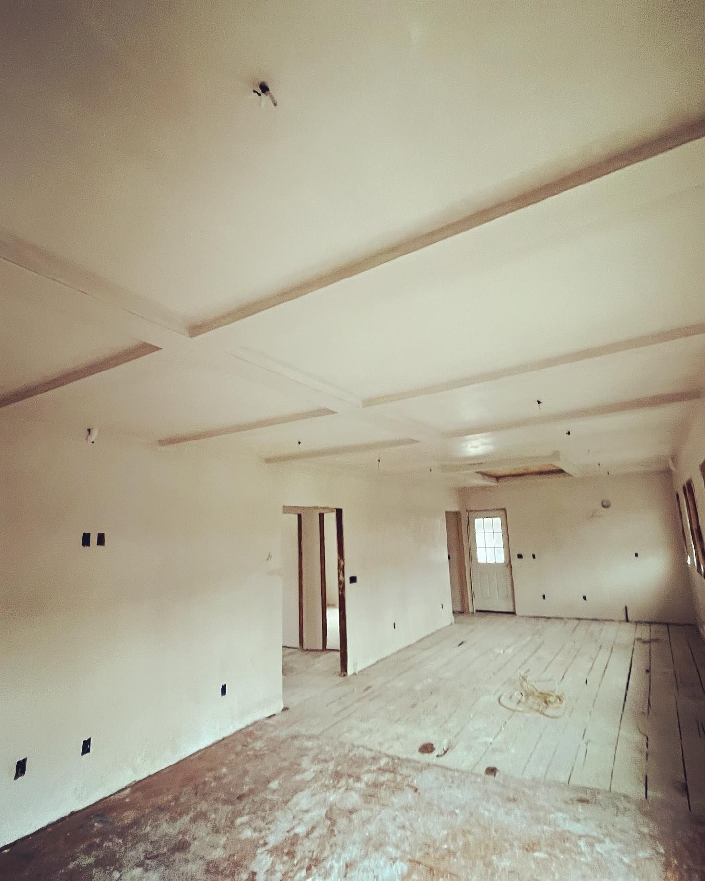 Unfinished interior with exposed beams and doorway, light walls, and wooden floor.