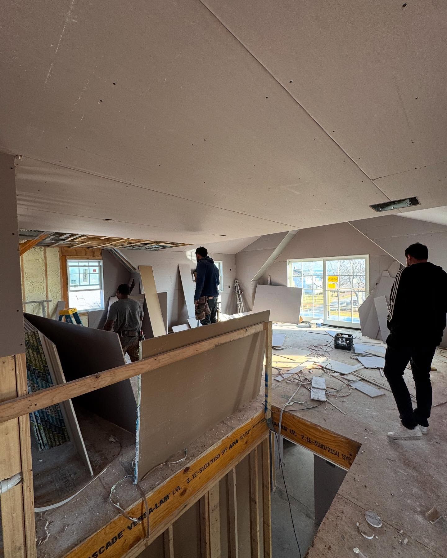 Construction site: Interior view of a room with drywall, workers, and debris.