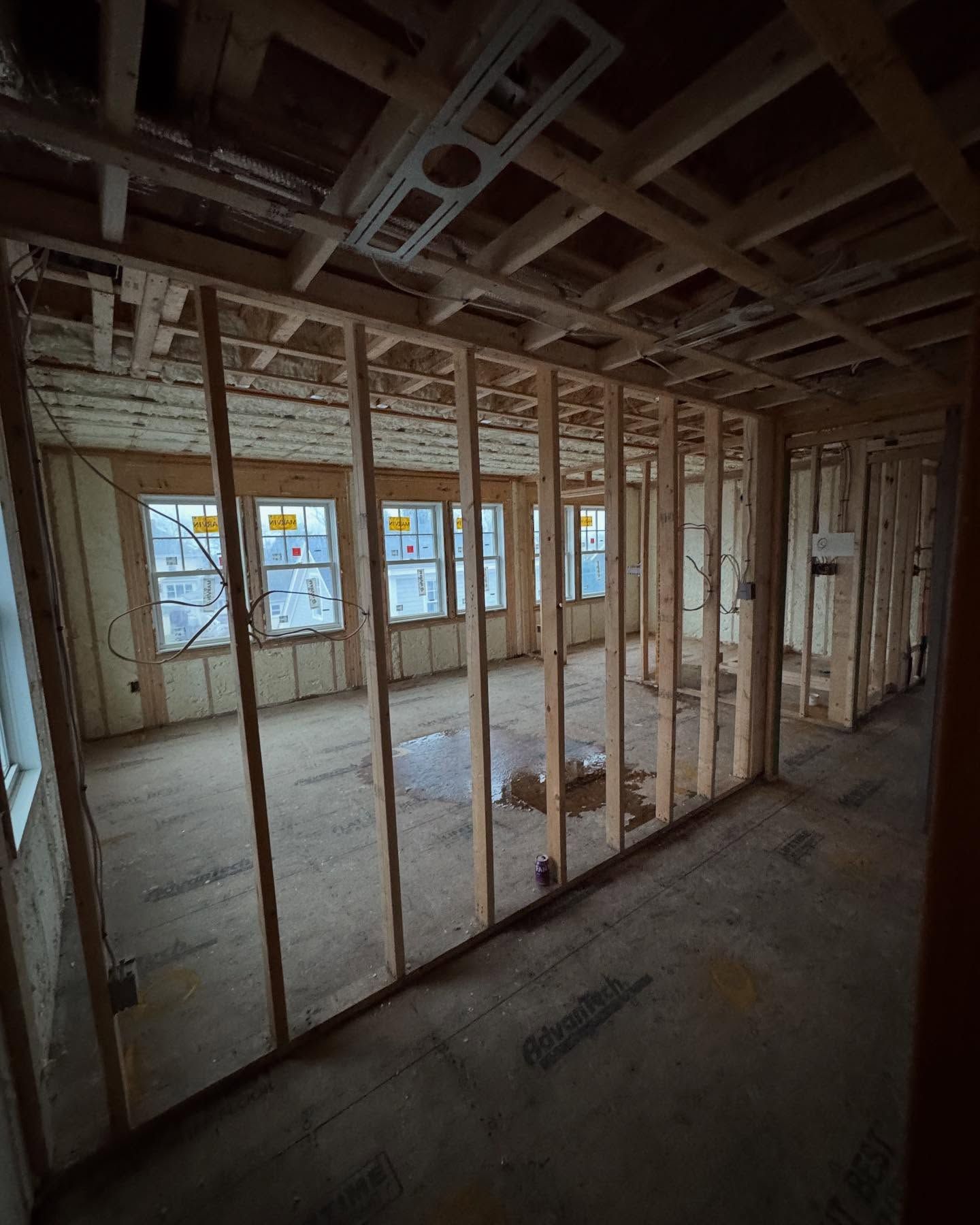 Interior of a house under construction, with wooden framing, windows, and spray foam insulation visible.