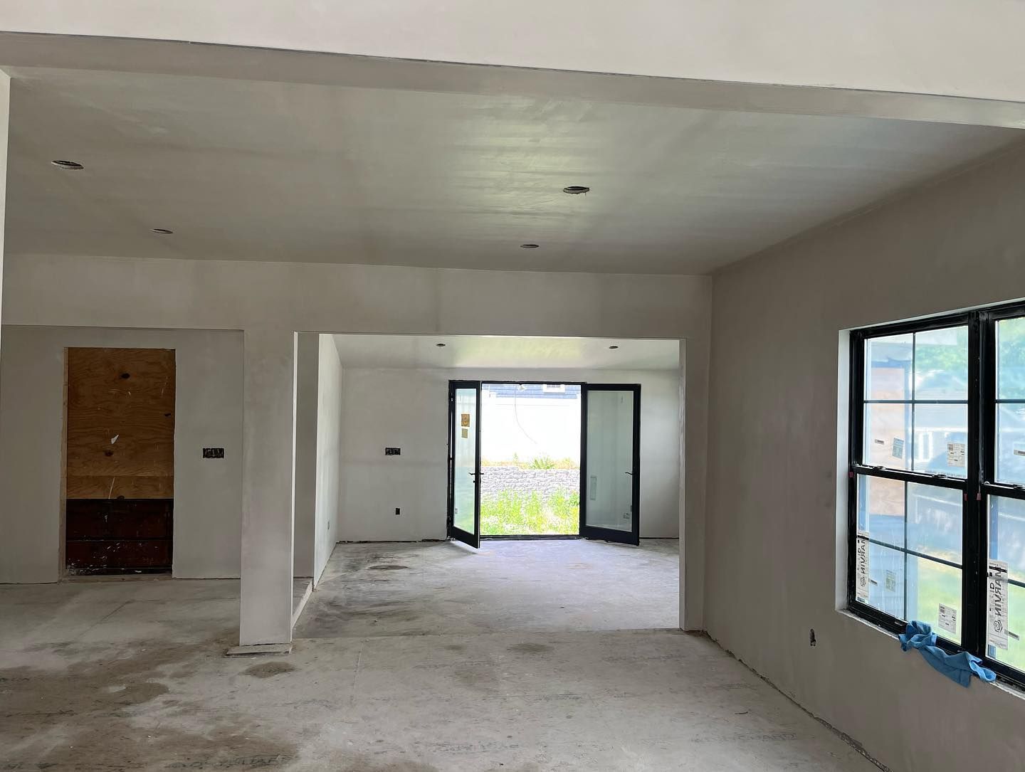 Interior view of a room under construction with white walls, concrete floor, and open doorways.