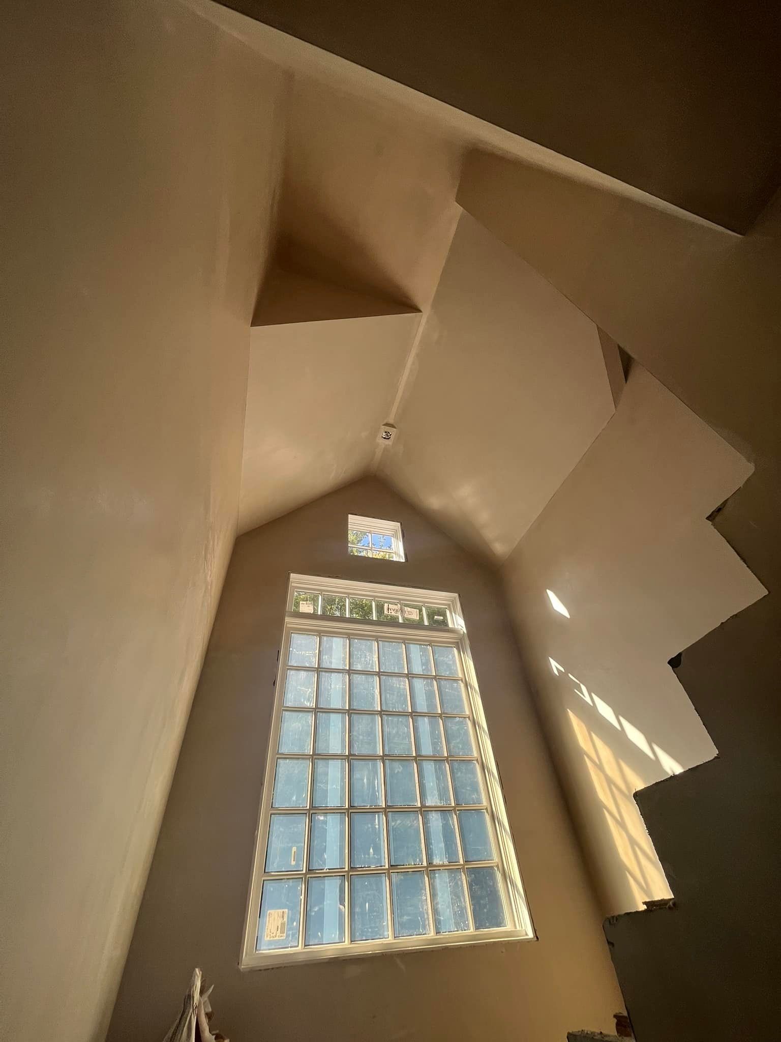 Interior view of a tall, angular room with a large window and stairs on the right side.