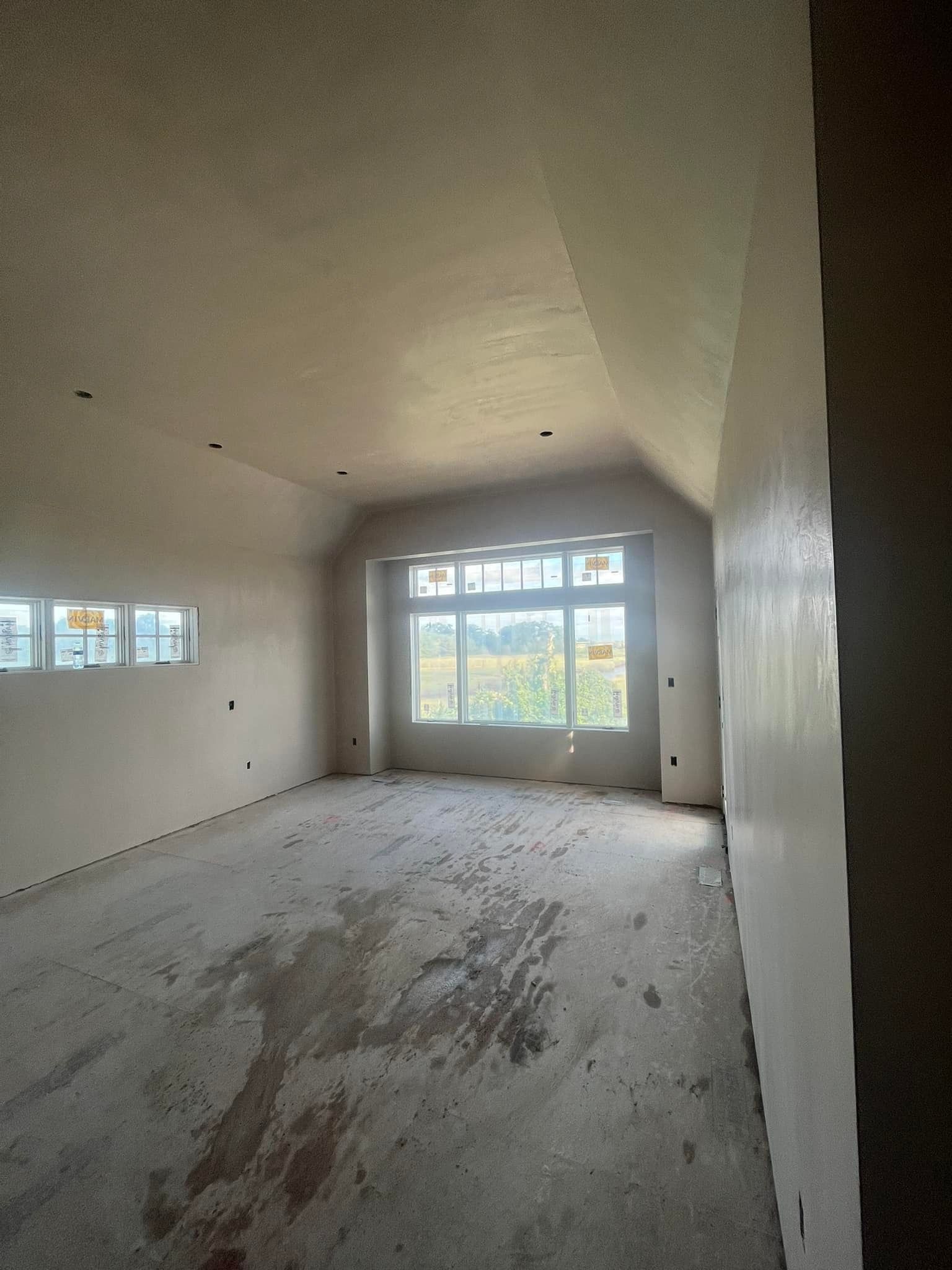 Interior view of an unfinished room with a window overlooking a landscape. Drywall, concrete floor, and natural light.