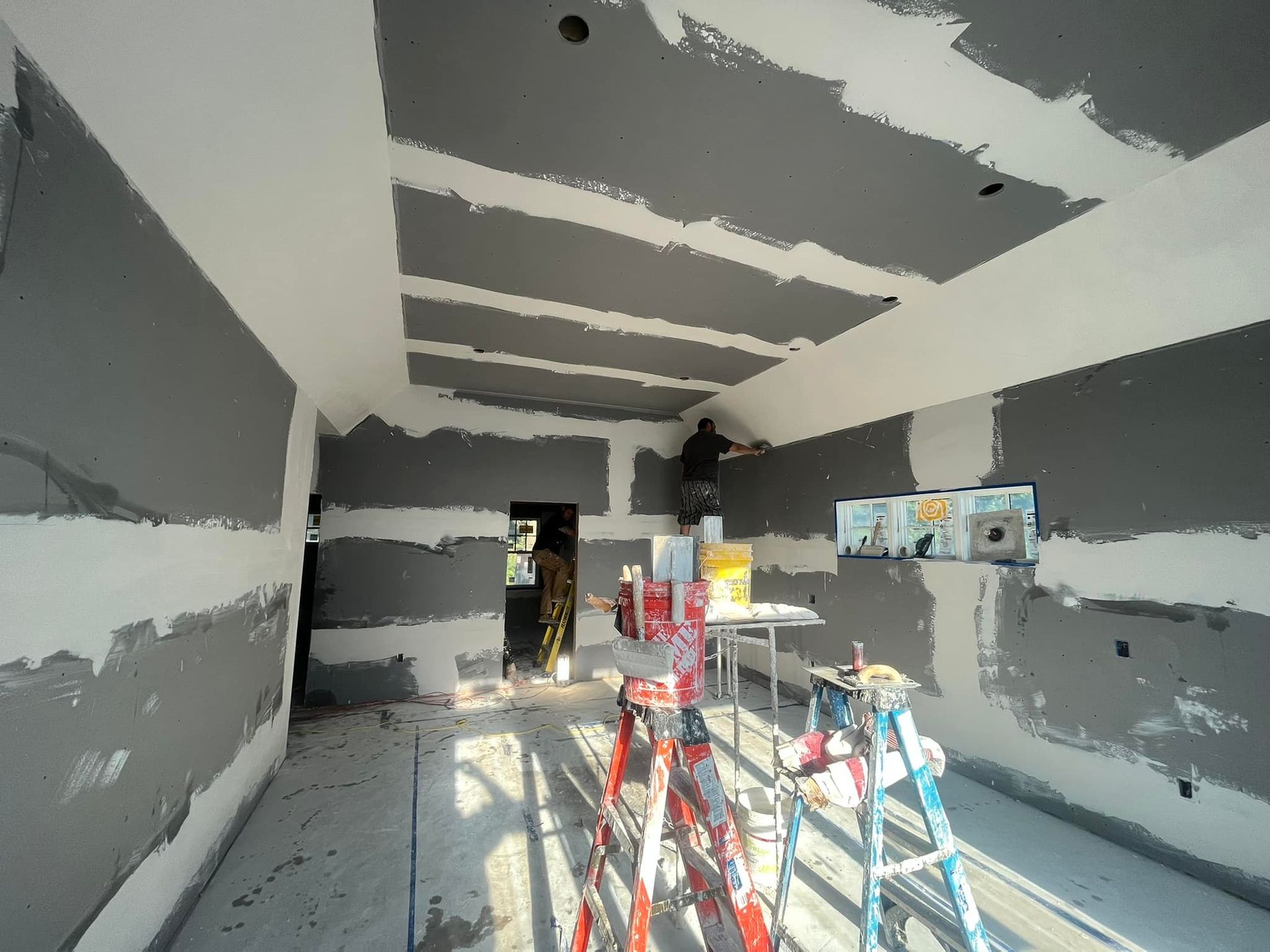 A room under construction, with gray drywall and a worker on a ladder.