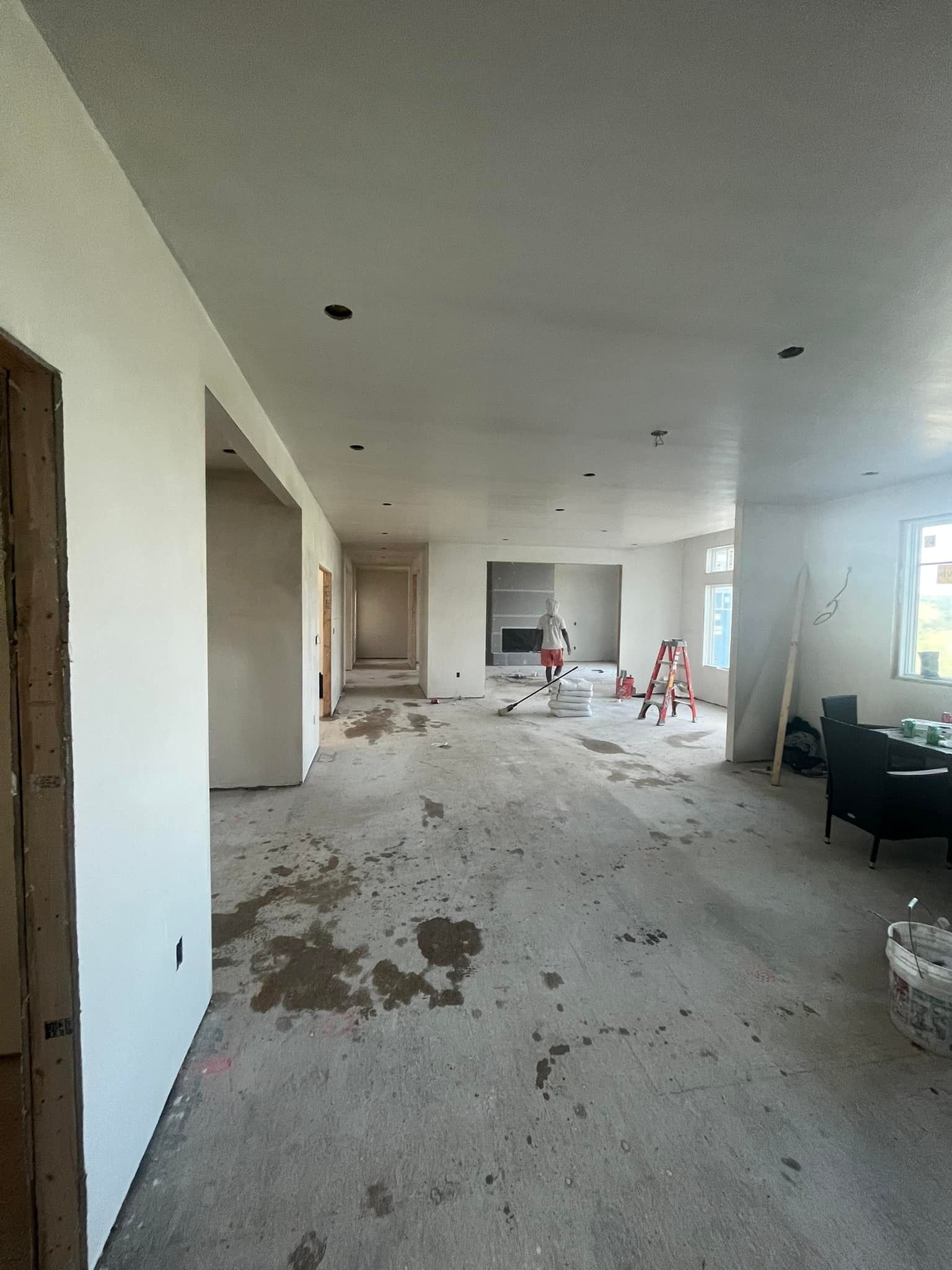 Interior under construction: bare concrete floor, white walls, unfinished doorways, and a fireplace.