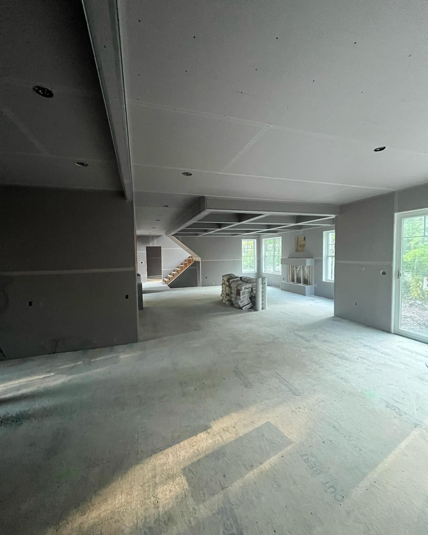 Interior of a room under construction, with gray walls, concrete floor, stairs, and windows.