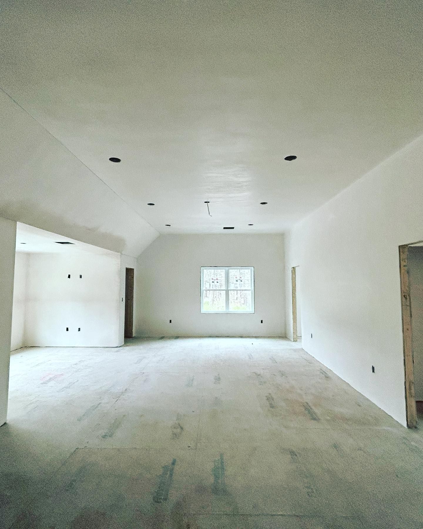 Empty room with white walls, window, and unfinished floor; under construction.