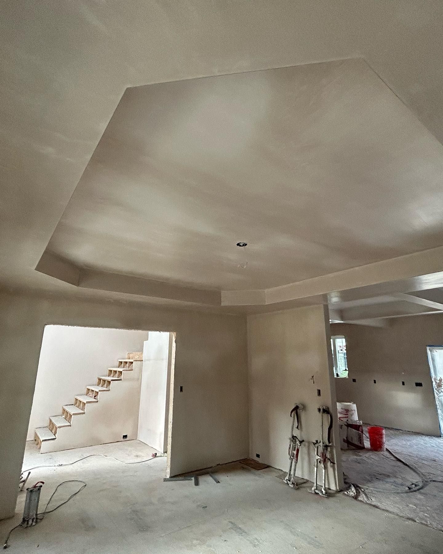 Interior view of a construction site with a textured ceiling, walls, and a staircase in the background.