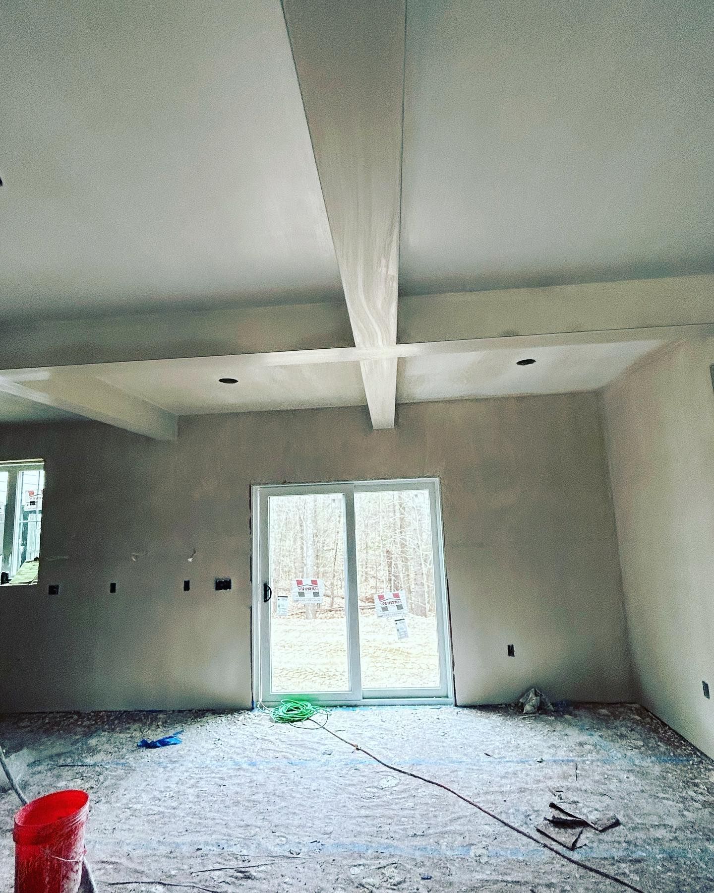 Interior of a room under construction, showing ceiling beams, unfinished walls, and a sliding glass door.