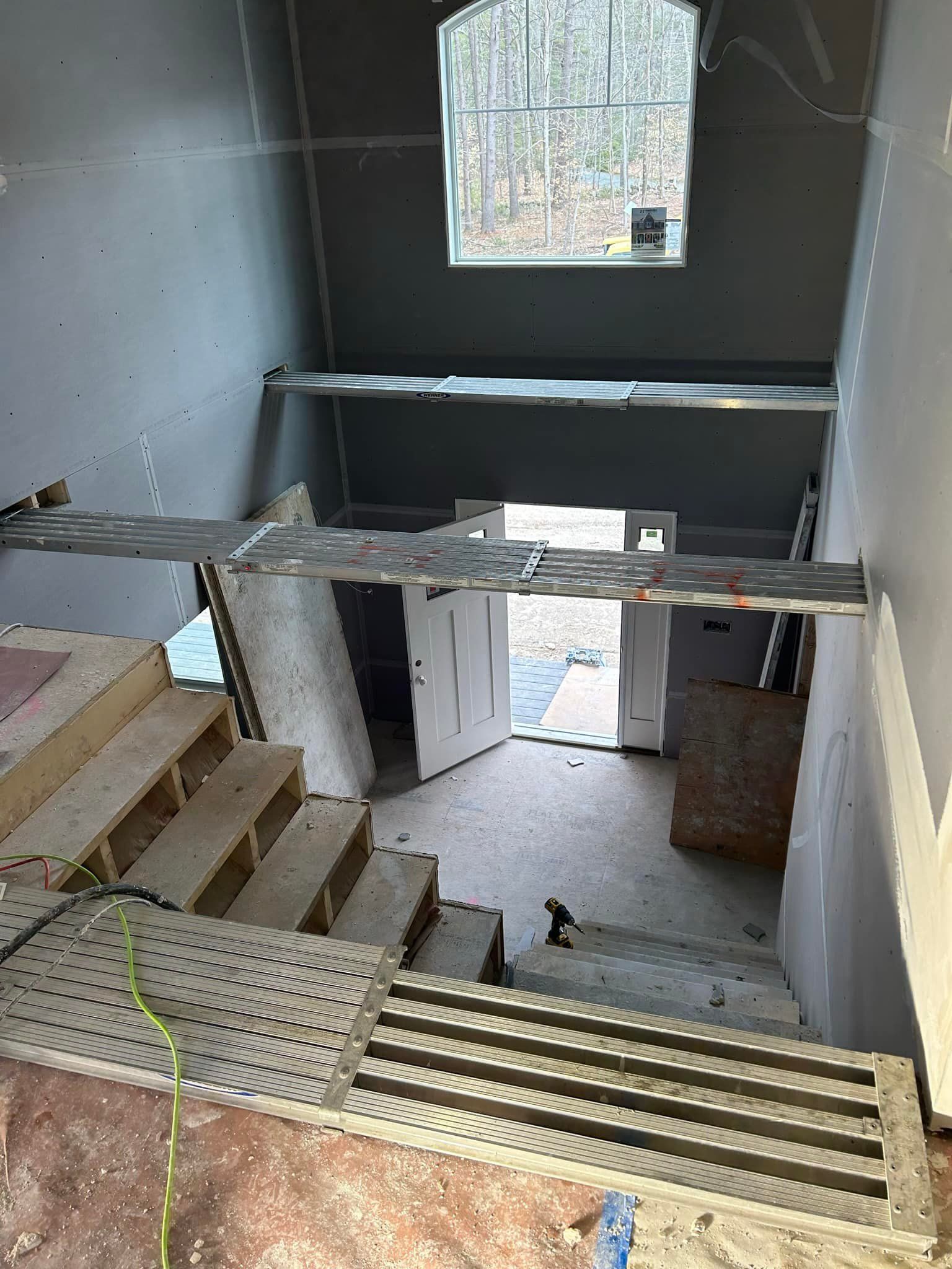Staircase under construction, leading down to a doorway, with scaffolding overhead, and a high window in the background.
