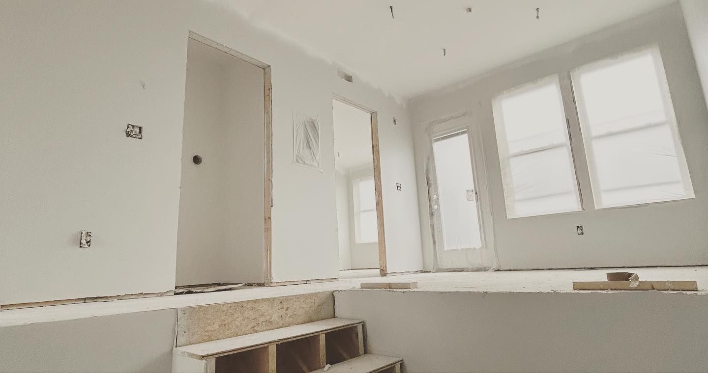 Interior under construction with stairs, doorways, and windows; walls are white.