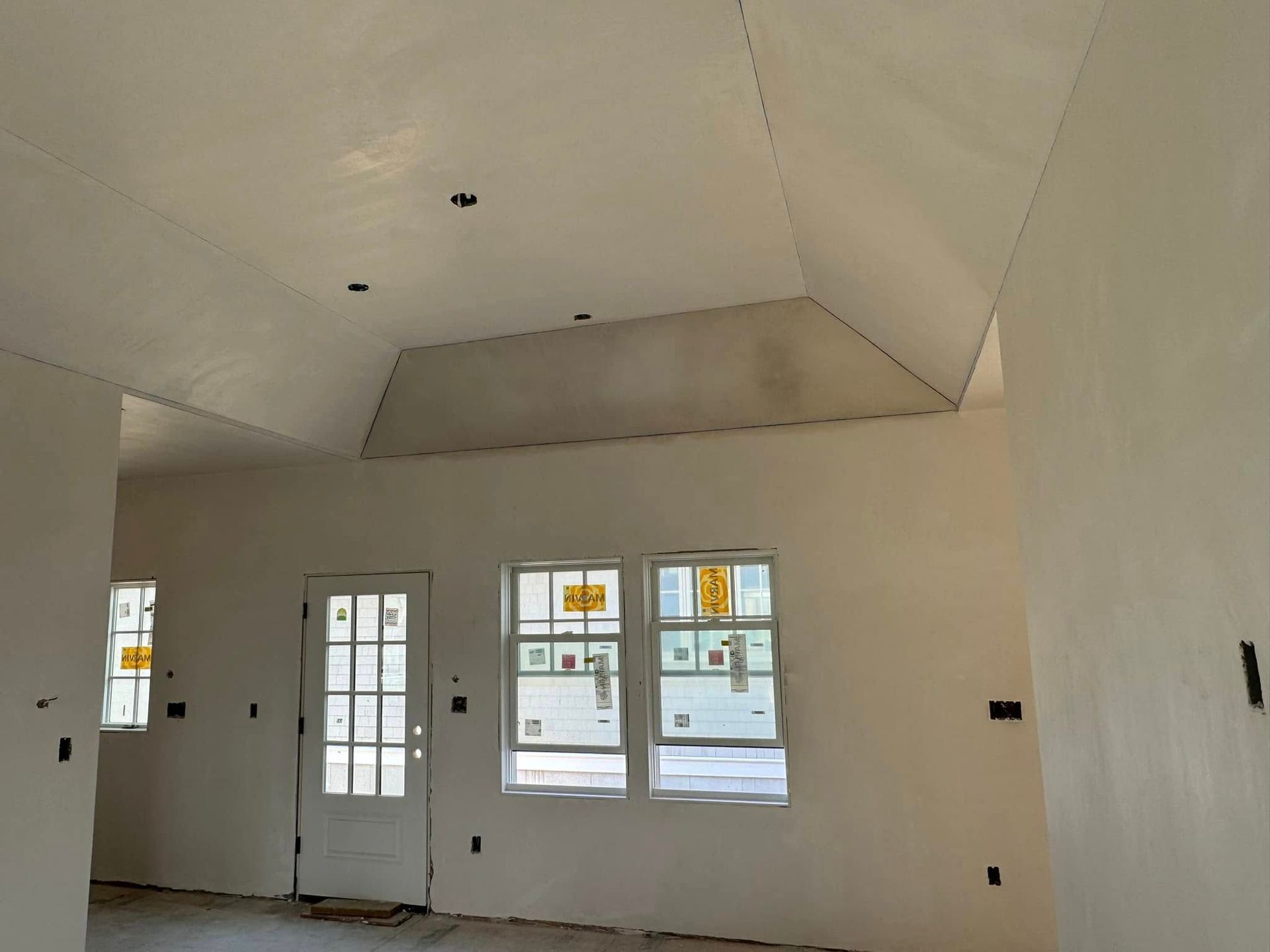 Interior view of a room under construction, with windows, a door, and an angled ceiling; walls are white.