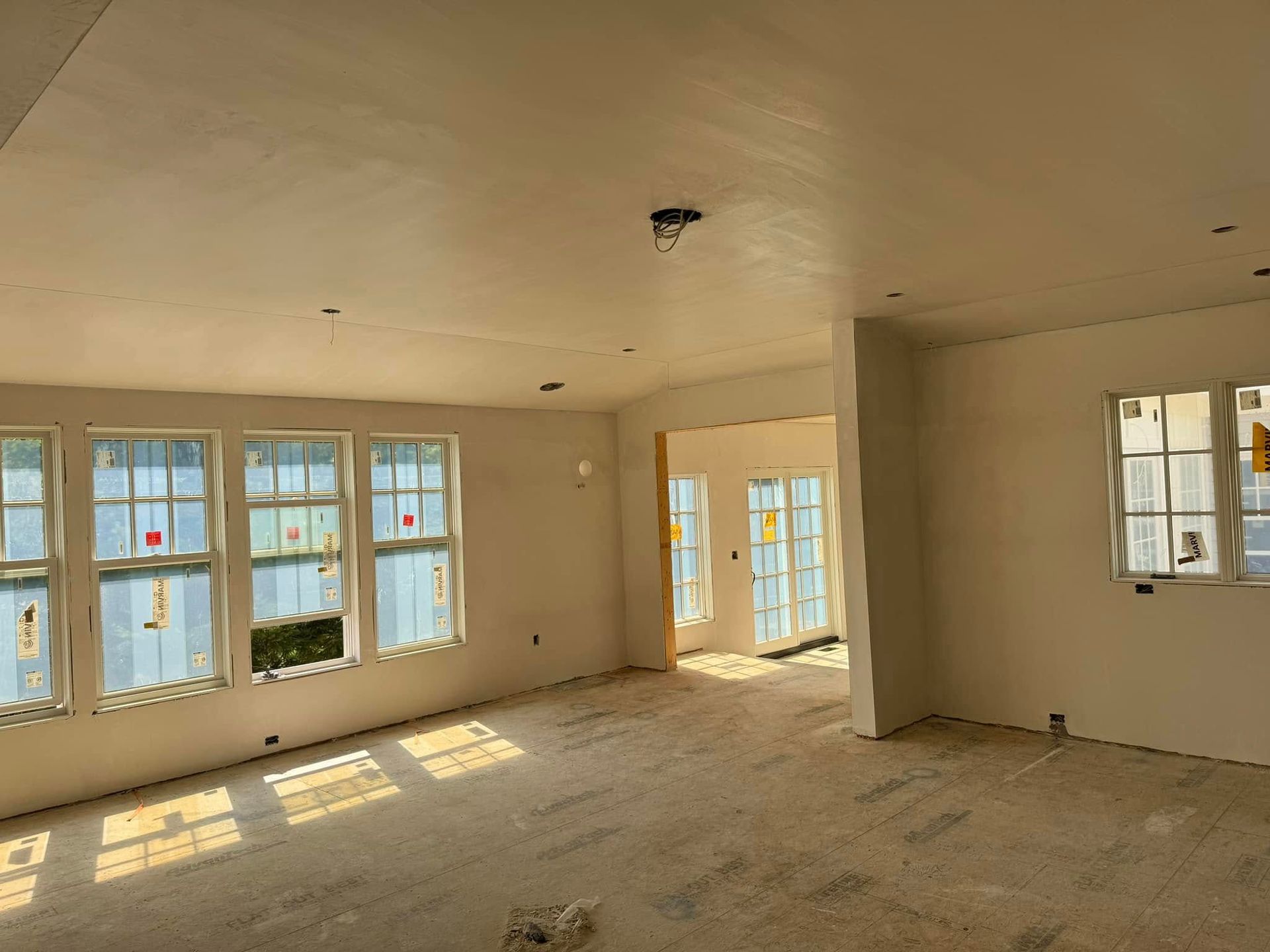 Interior of a room under construction with white walls, multiple windows, and an open doorway.
