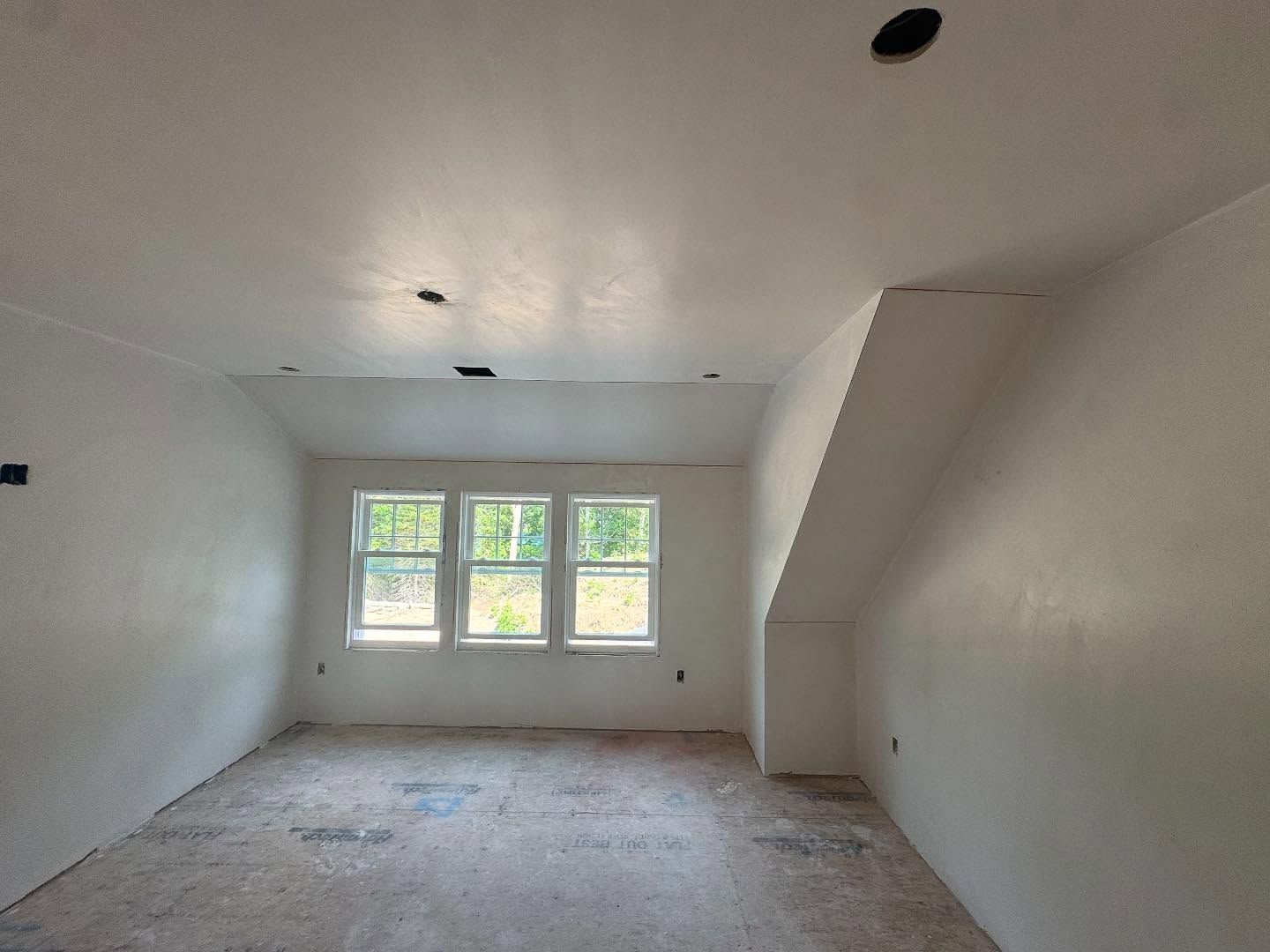 An empty, white-walled room with a window and slanted ceiling, under construction.