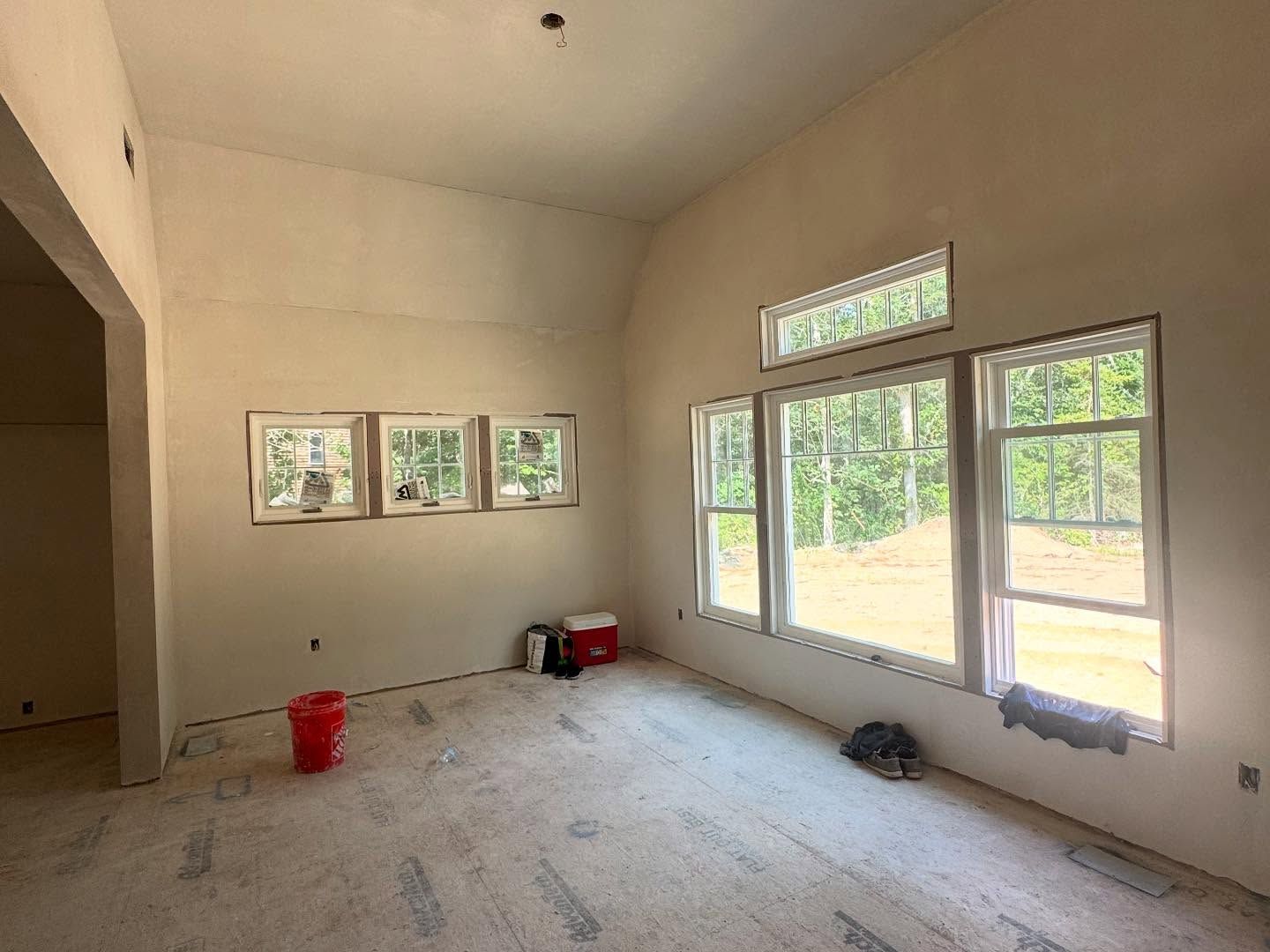 Interior of a room under construction with several windows, neutral walls, and a bare concrete floor.