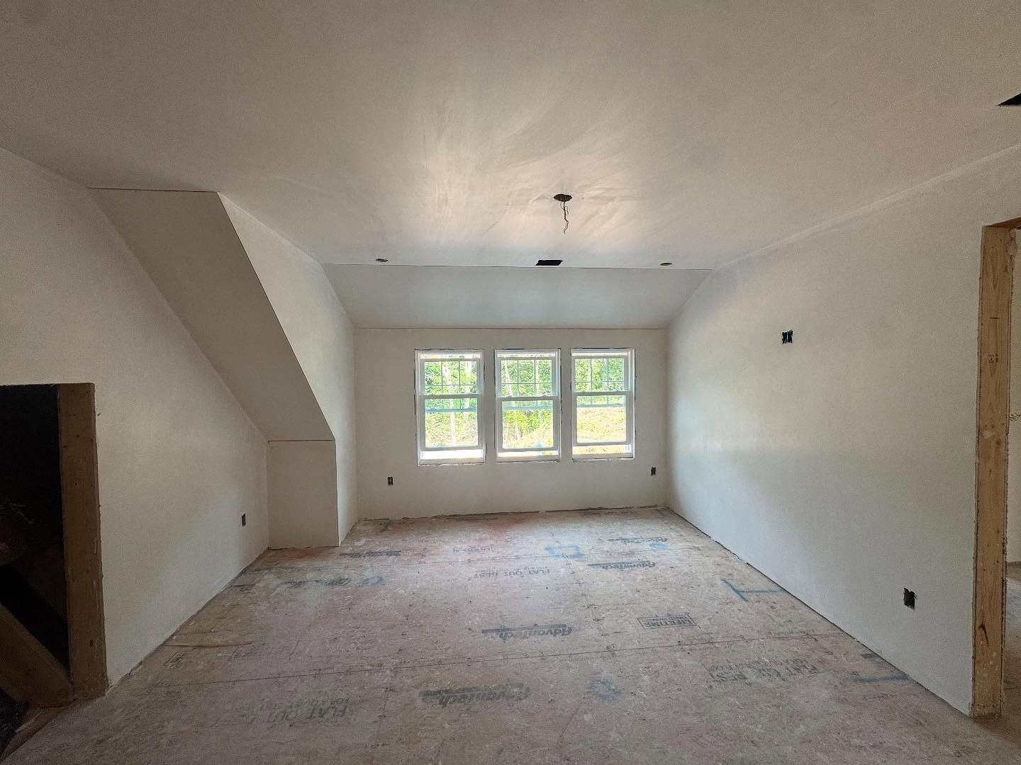 Interior of a room under construction with white walls, windows, and an unfinished floor.