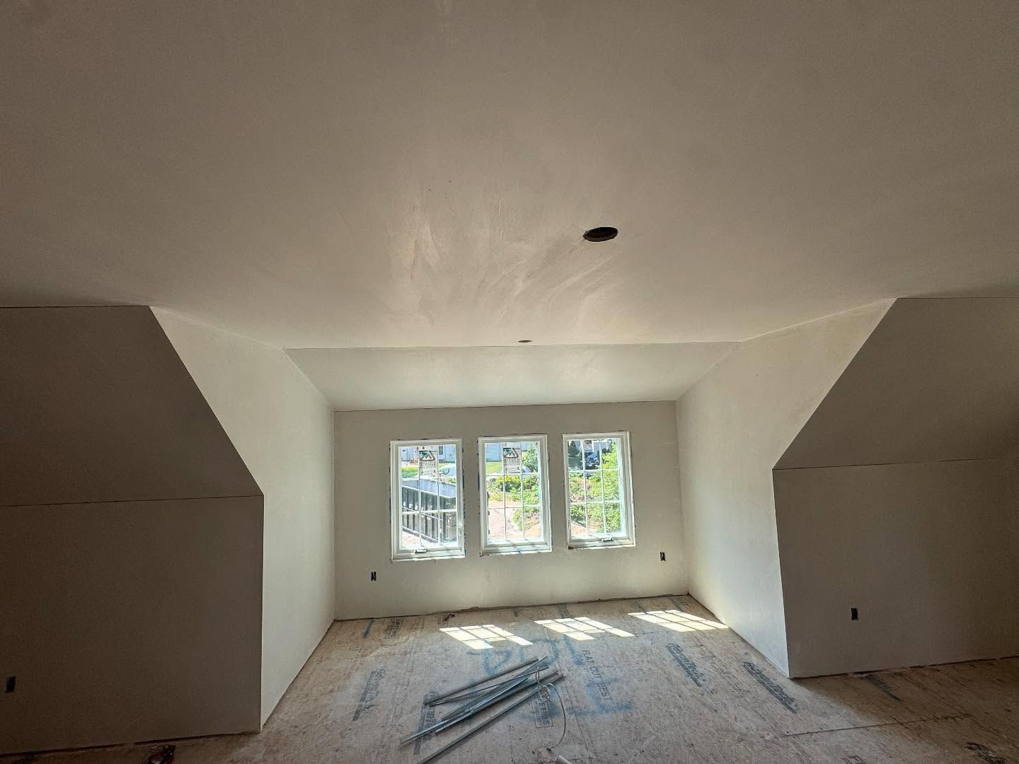 Interior of a room under construction, featuring three windows, angled walls, and bare flooring.