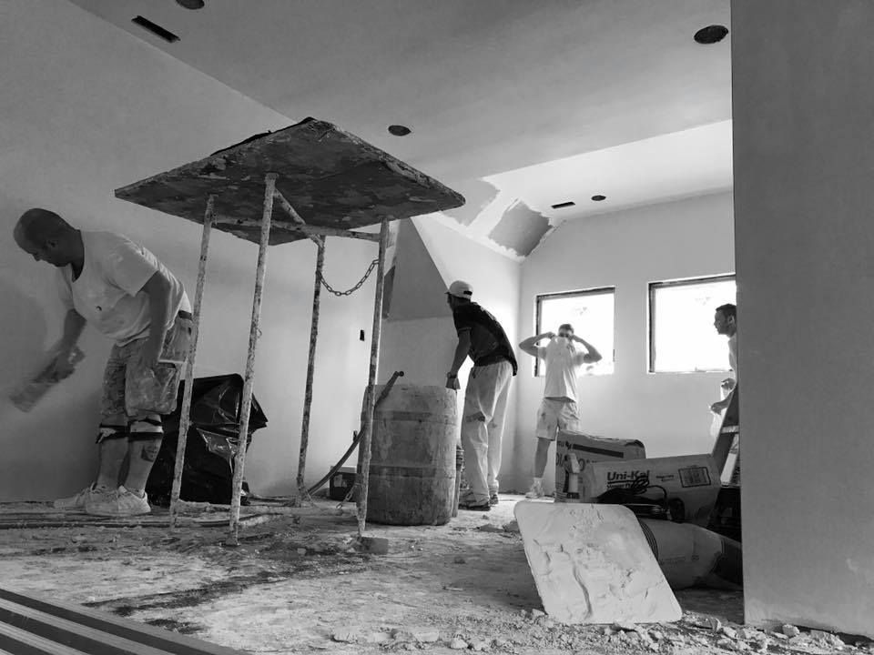 Construction workers painting the interior of a room with a makeshift protective covering in the center.