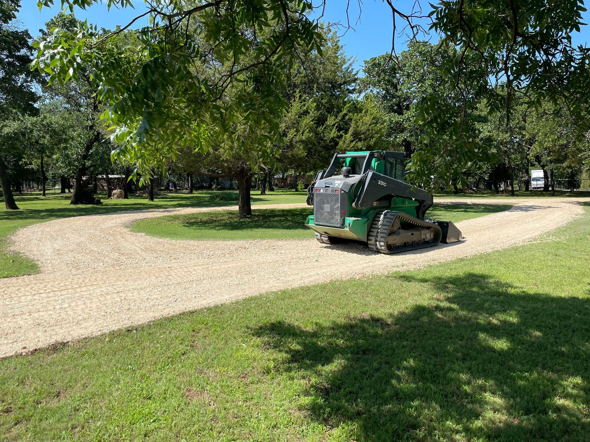 A green bulldozer is driving down a gravel road in a park.