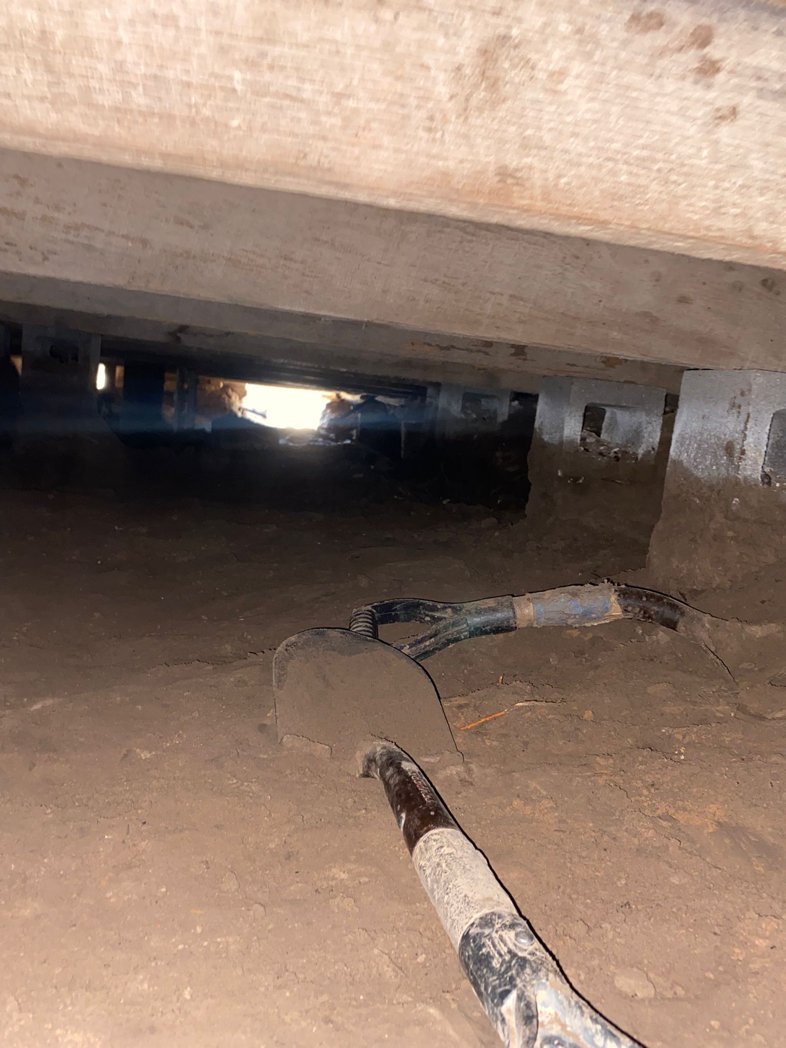 A hose is laying on the ground under a concrete structure.