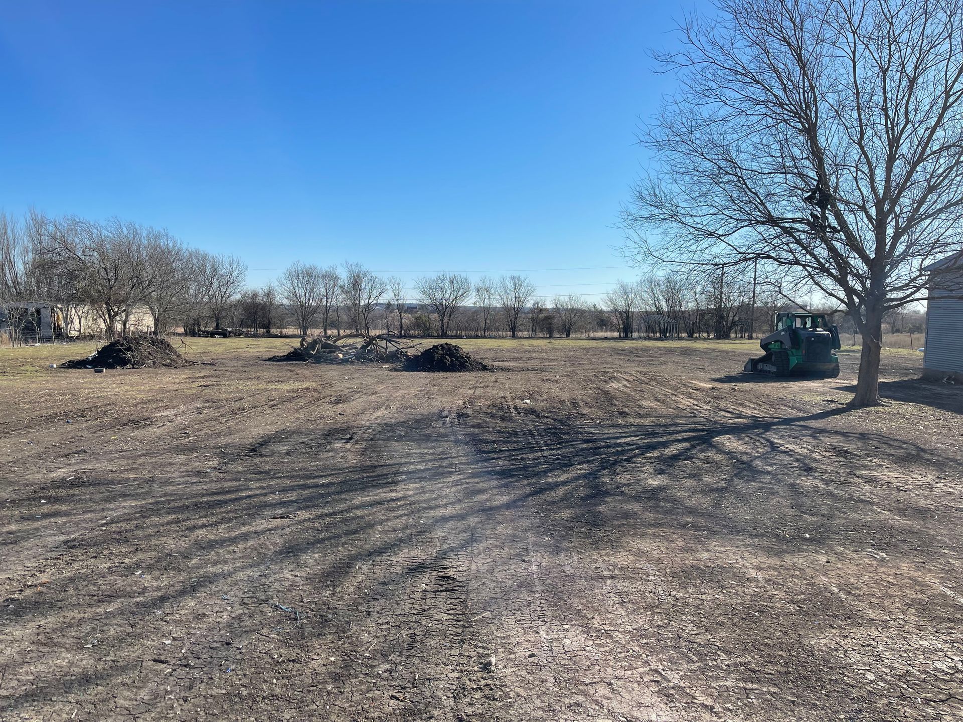 A tractor is driving through a dirt field with trees in the background.