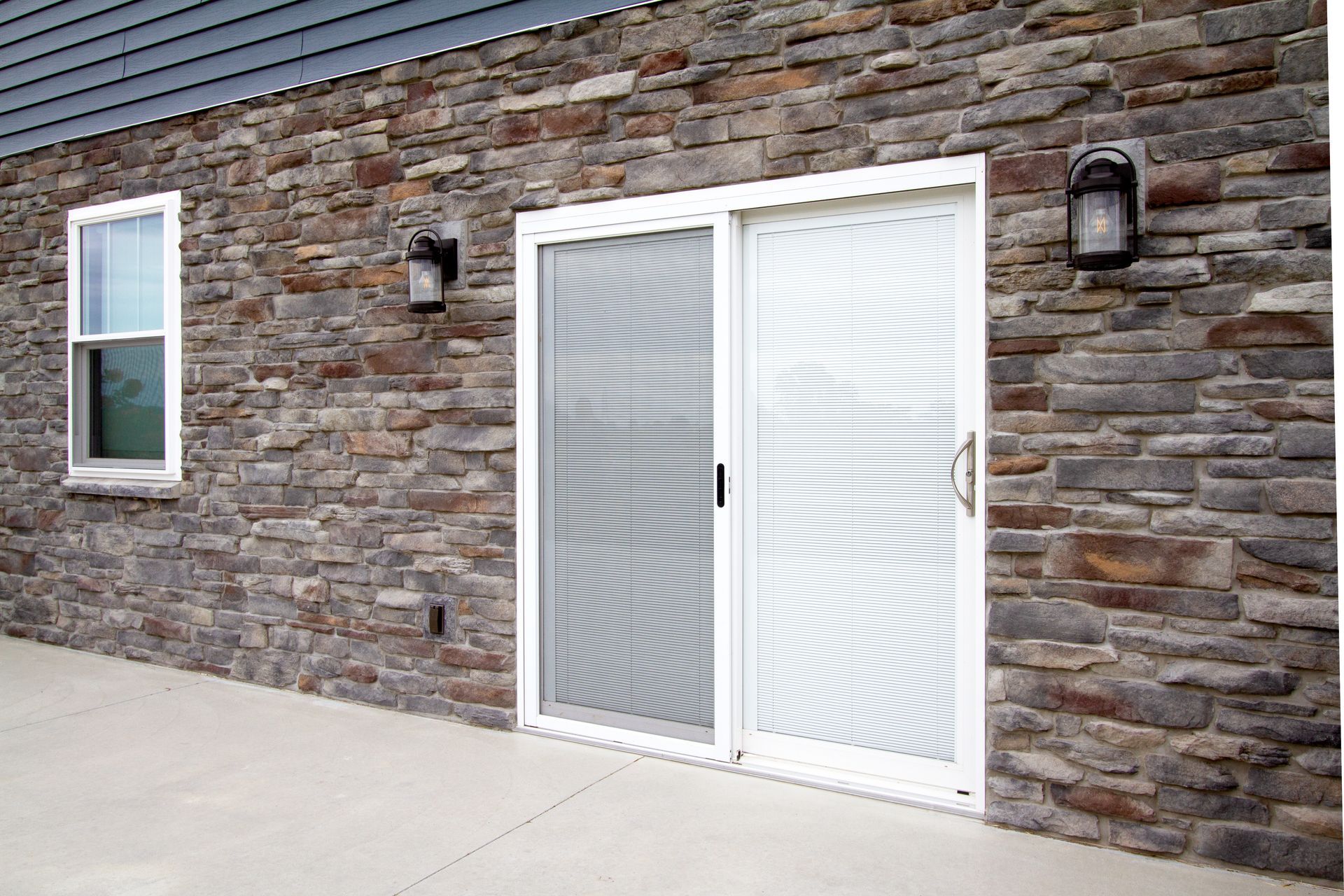 Exterior of building with stone veneer walls, sliding glass door, and window.