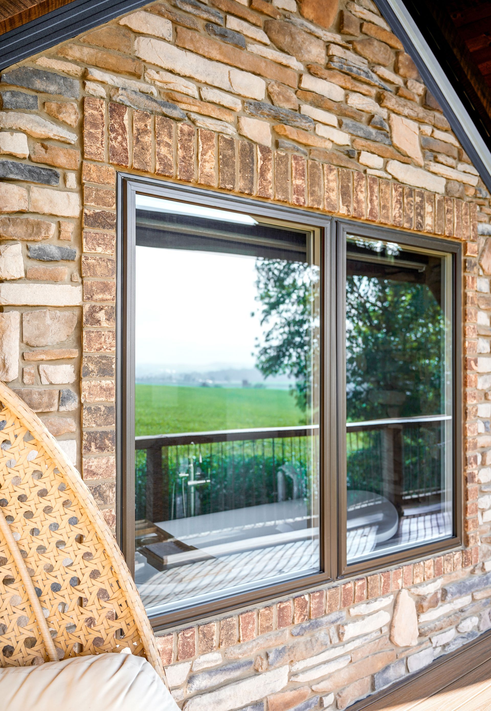 Large window framed by brick and stone, overlooking a deck and green landscape.