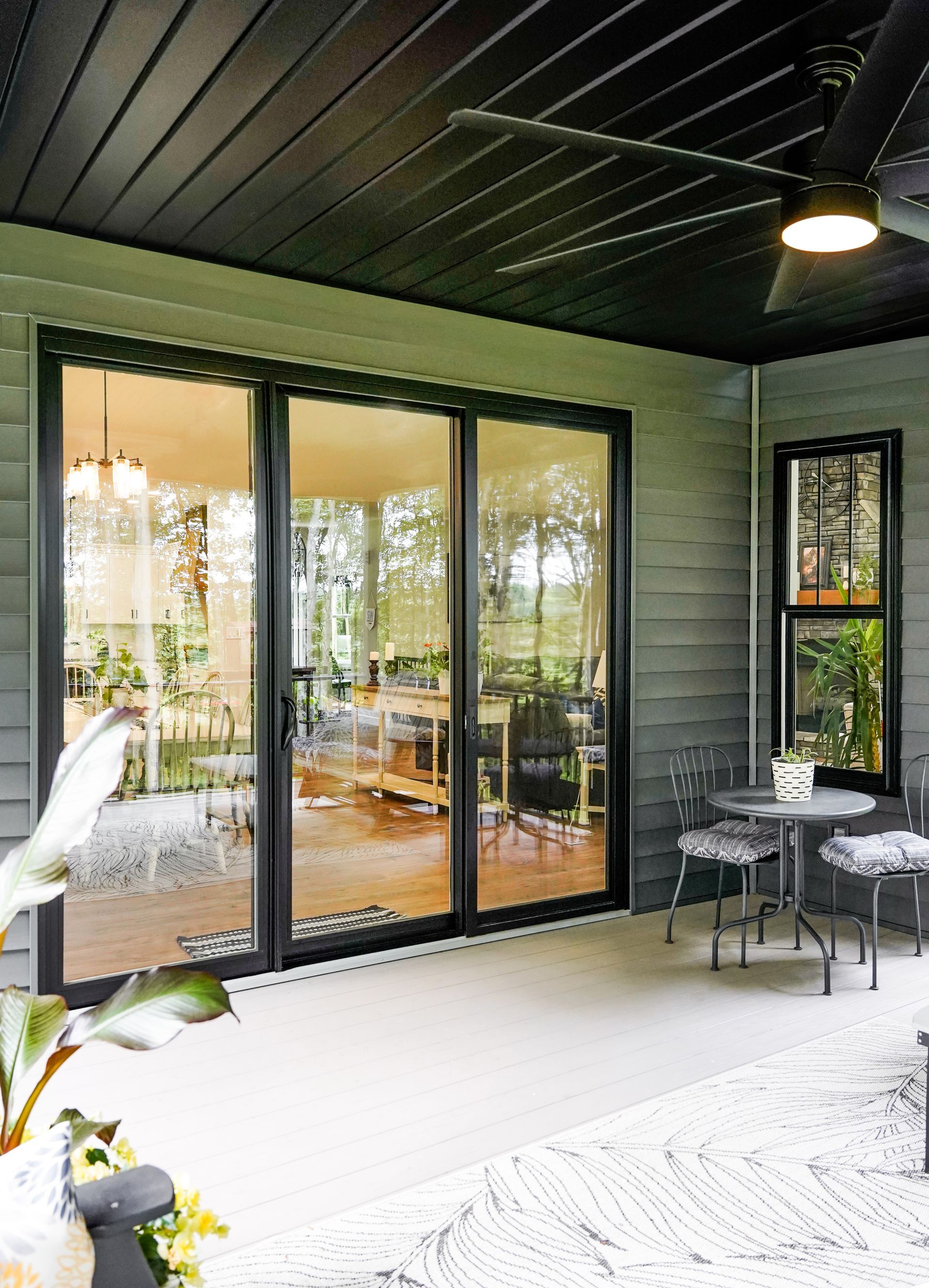 Patio with sliding glass doors, black ceiling and trim, small table and chairs, and a ceiling fan.