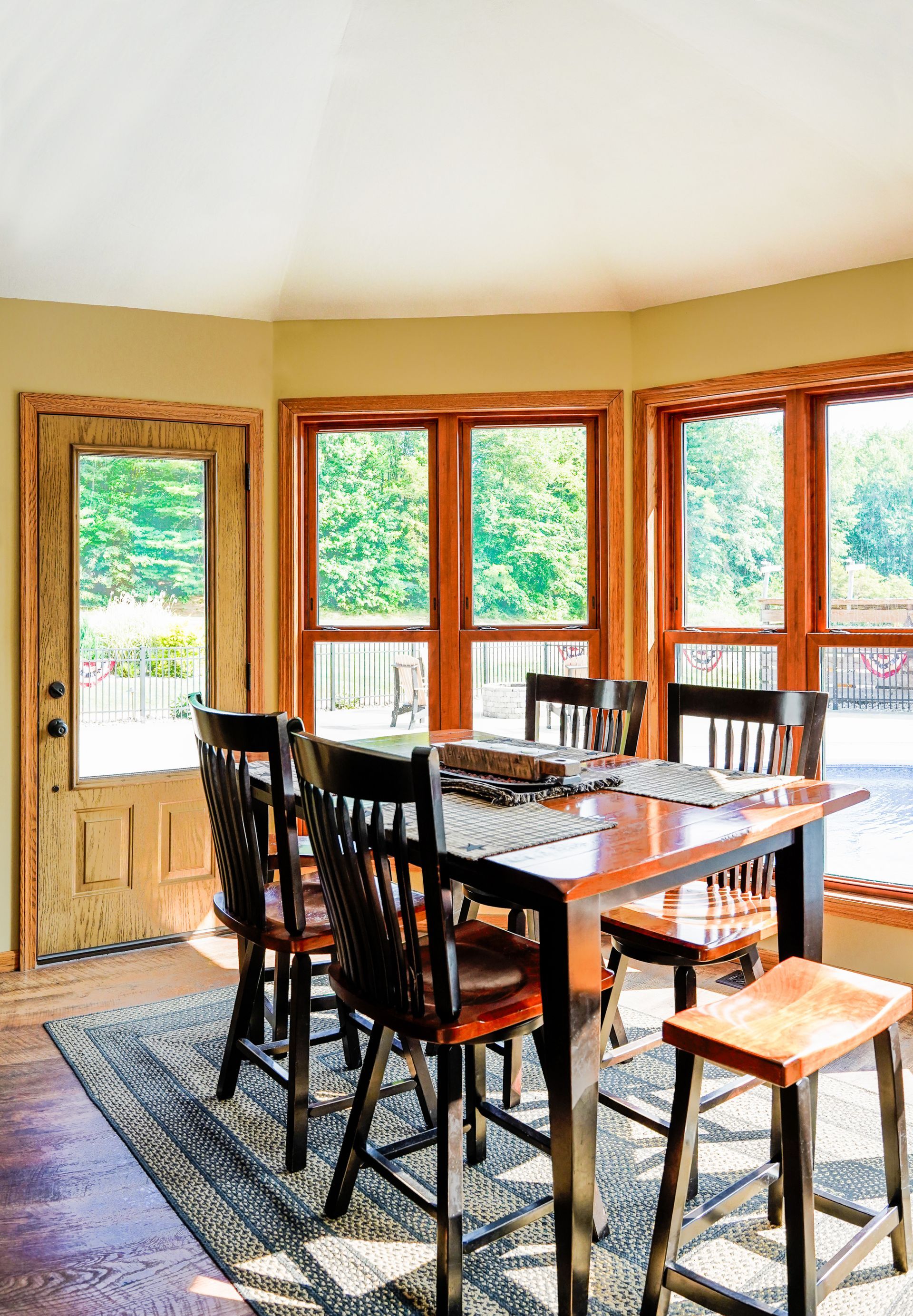 Dining room with wooden table and chairs, sunlight through windows.