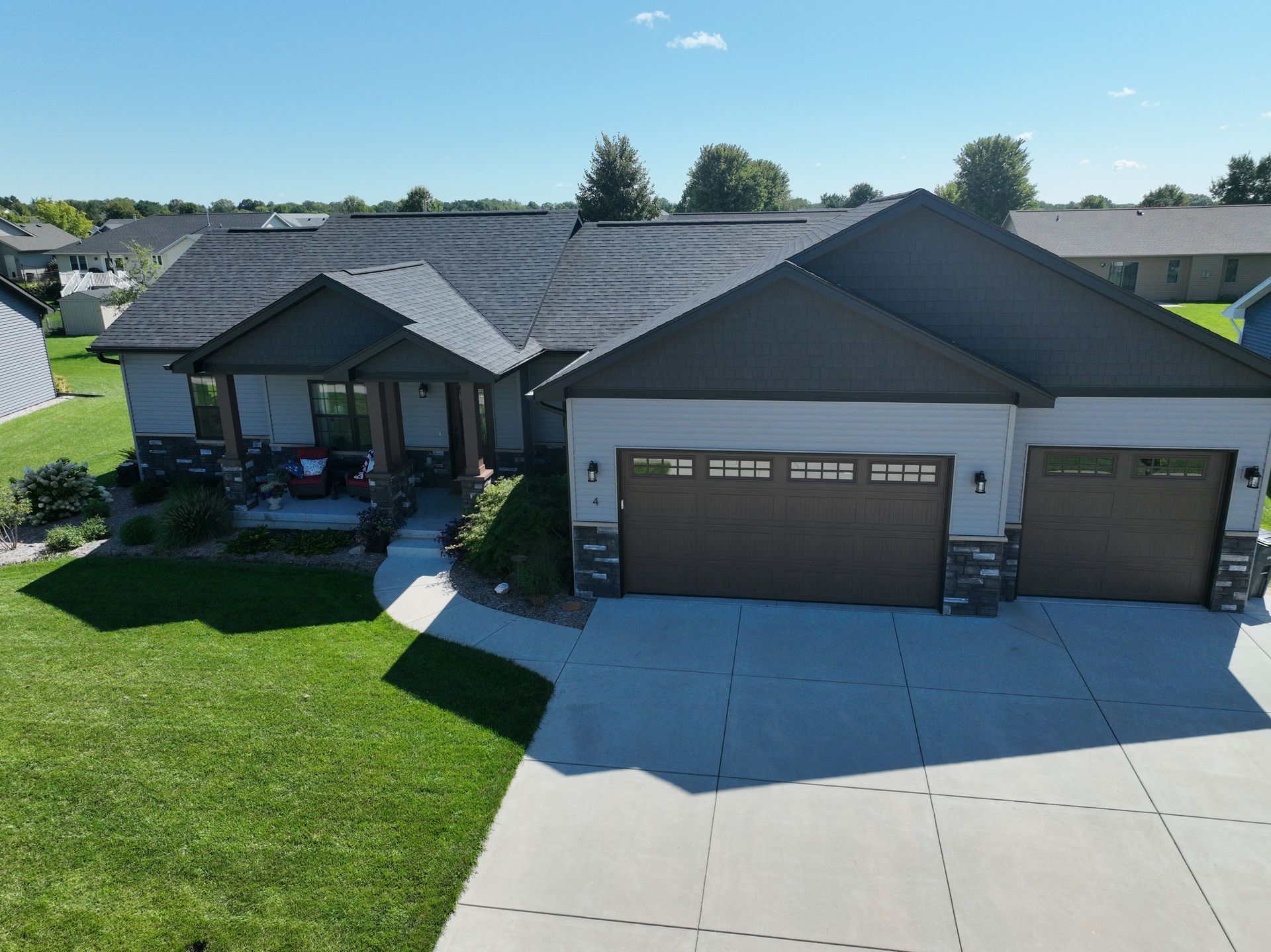 Aerial view of a single-story light gray house with a dark gabled roof, two-car garage, and a front porch.