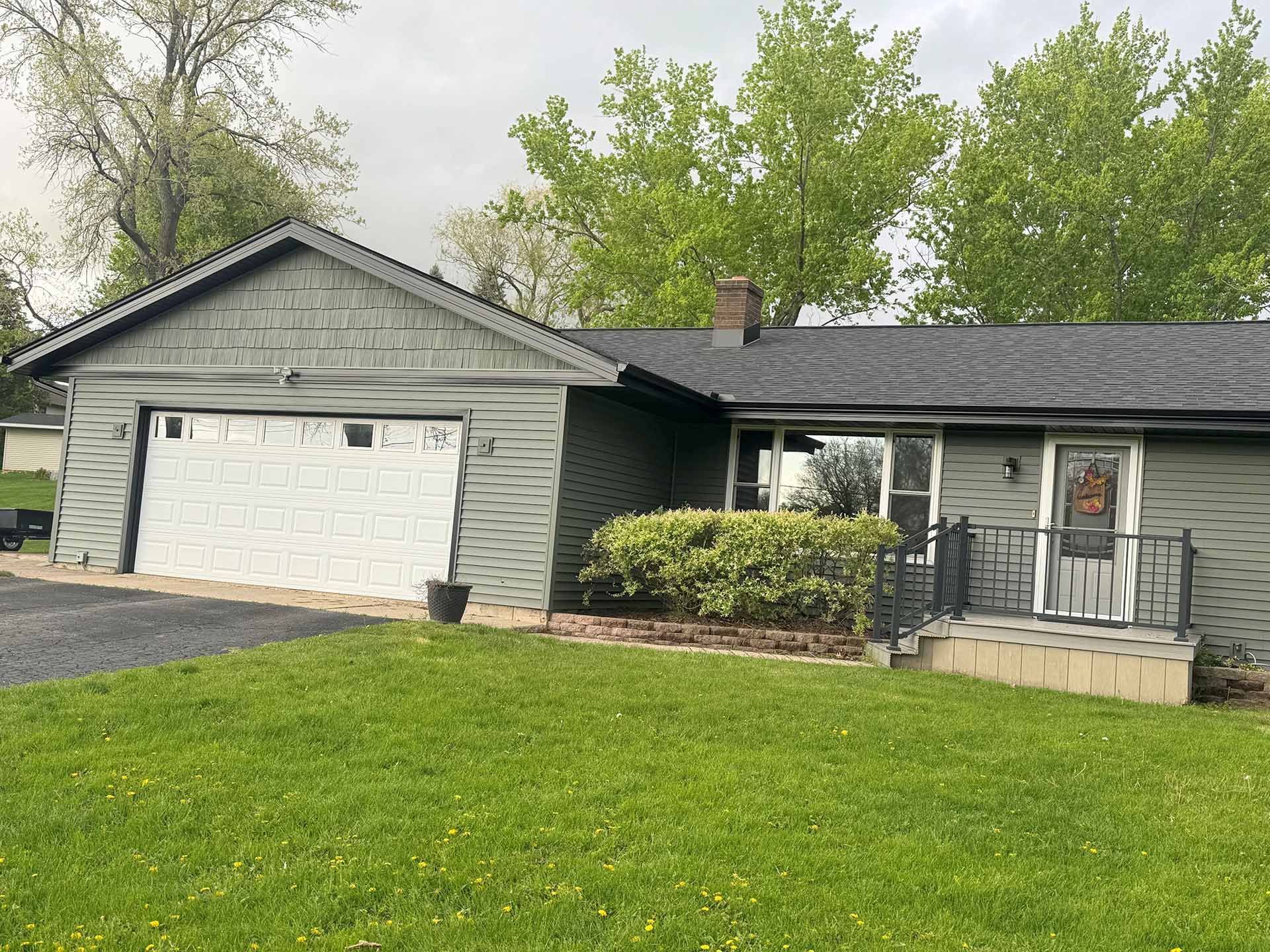 Single-story gray house with white garage, black roof, and green lawn in front