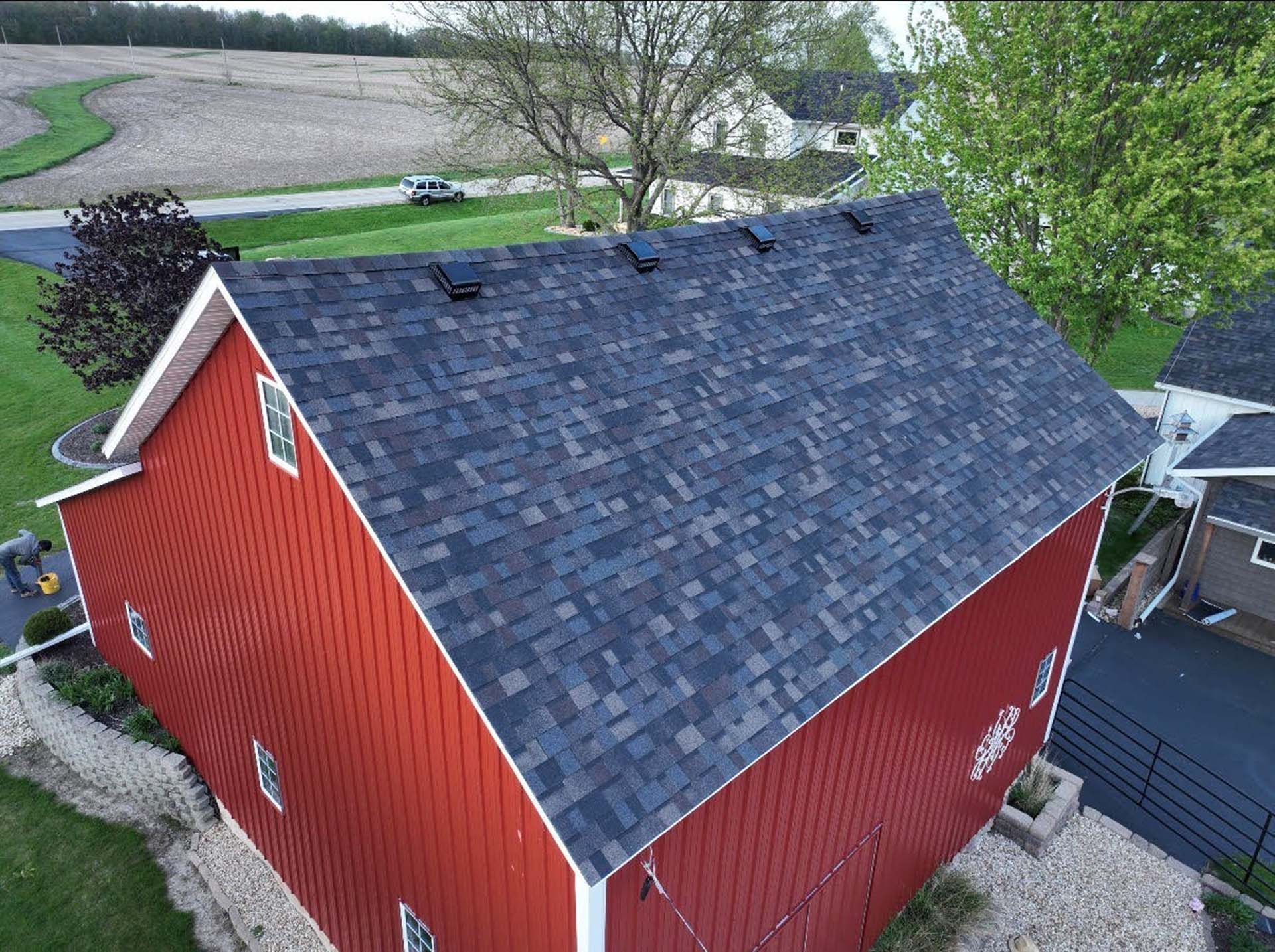 Red barn with dark shingled roof beside a driveway and fields