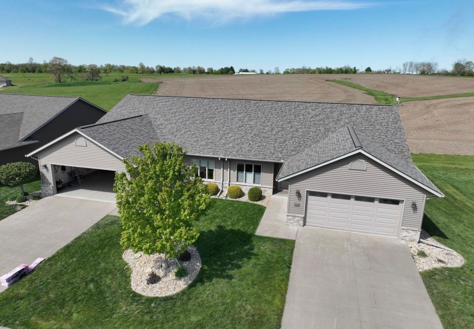 Aerial view of a gray-roofed suburban house with a driveway, lawn, and tree in front