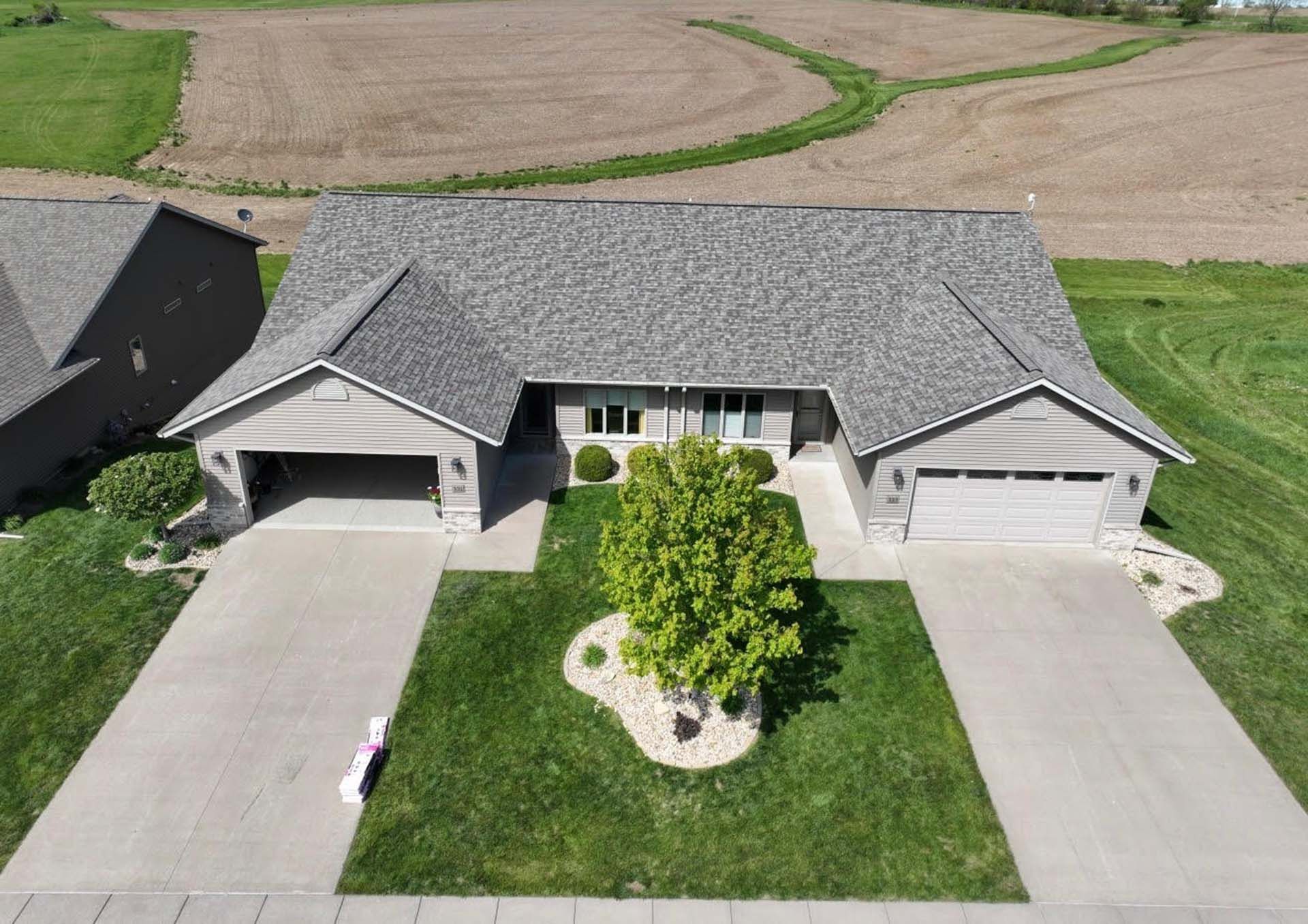 Aerial view of a gray suburban house with a two-car garage, driveway, and front lawn