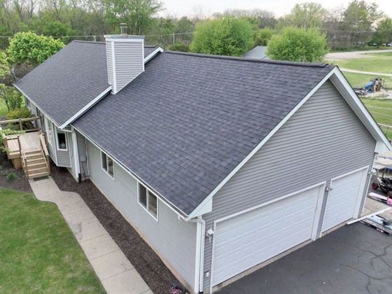 Aerial view of a gray house with dark roof, white garage, and trees around it