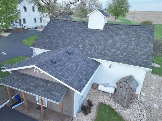 Aerial view of a house with a dark shingled roof, white siding, and a small porch