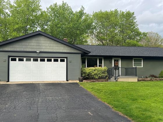Single-story green house with white garage, black driveway, and front lawn