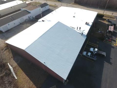 Aerial view of a commercial building with a roof partially covered in white membrane and partially with gray shingles.