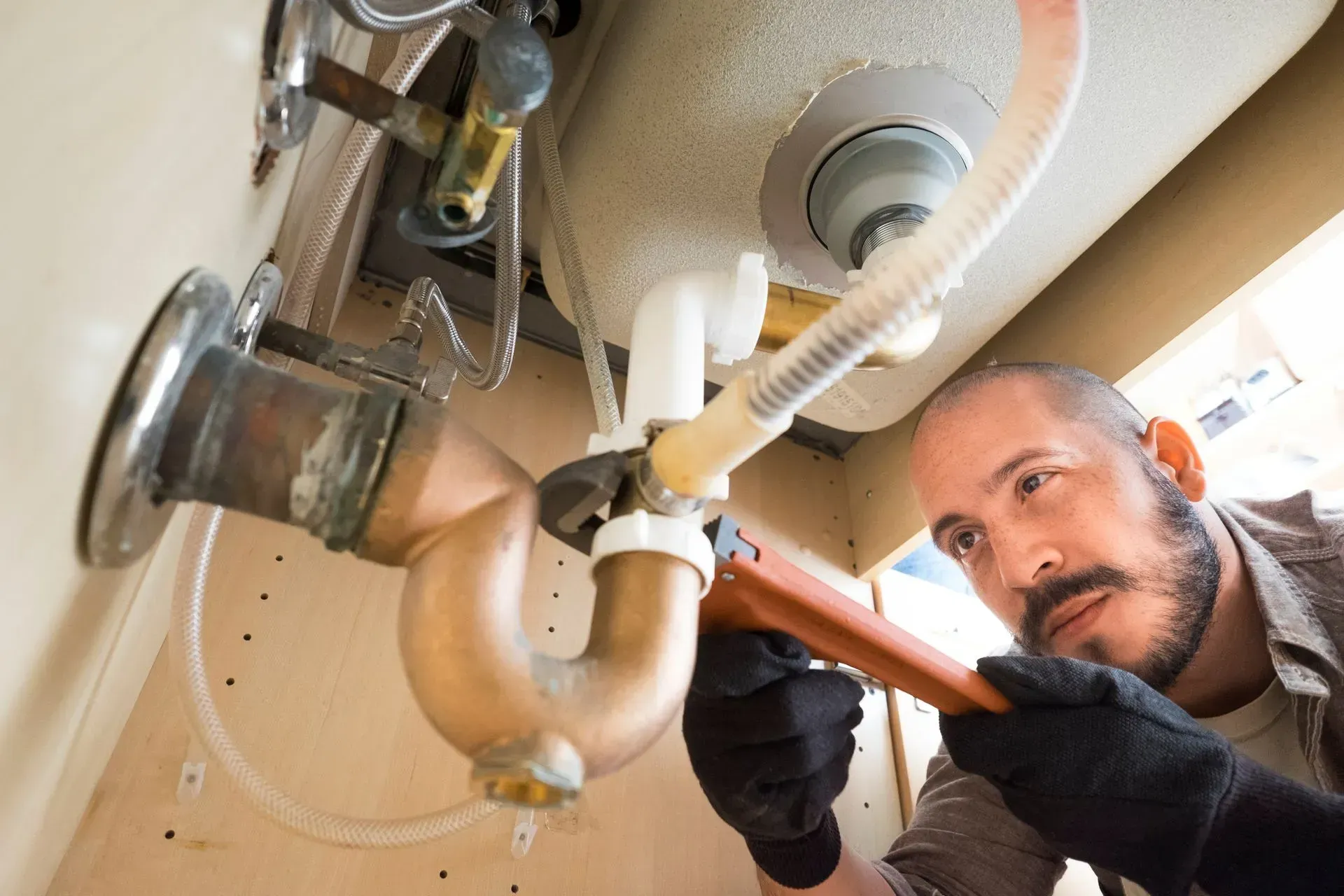 A man is fixing a sink pipe with a wrench.