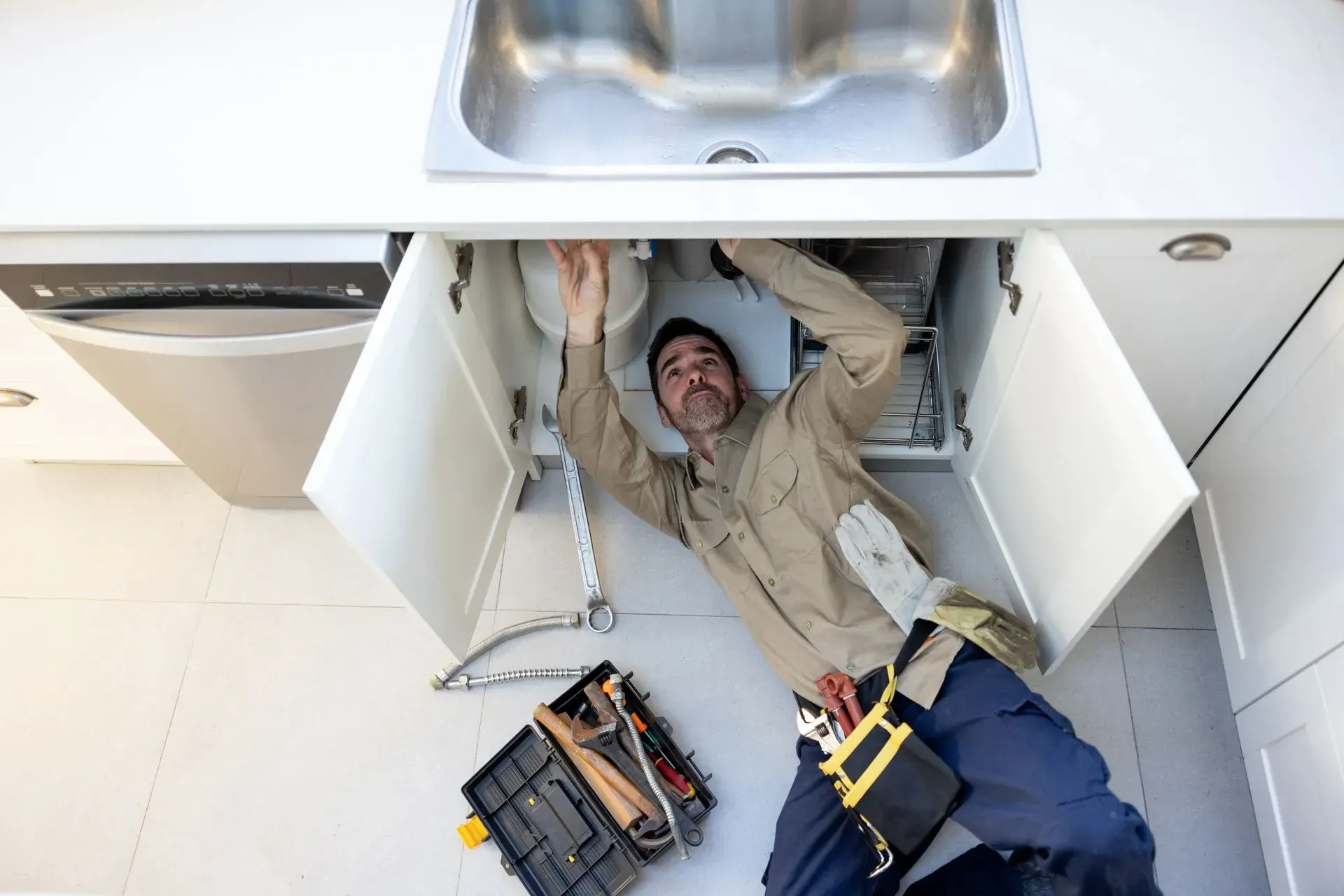 A man is laying on the floor under a kitchen sink