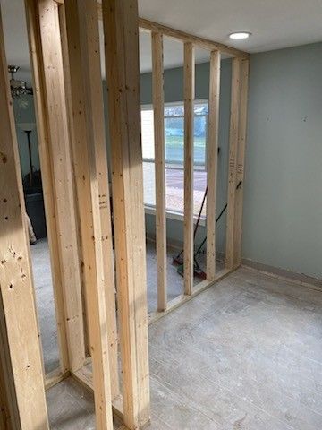 Interior view of a residential room renovation, featuring newly constructed wooden wall framing studs on a concrete floor.