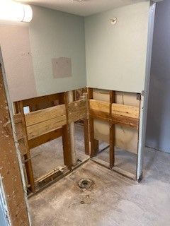 An interior view of a room under construction, showing wooden wall framing and a drain pipe on a concrete subfloor.